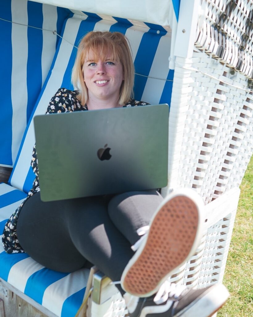 Maren Thiel, Social Media Managerin aus Nordfriesland, arbeitet lächelnd mit Laptop in einem Strandkorb